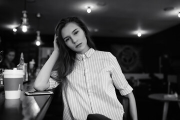 Fototapeta premium Girl with coffee. Young beautiful girl is sitting in a cafe and drinking coffee in a paper cup. The girl is having breakfast in the coffee house.