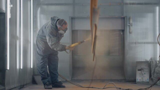 A man in a respirator is painting metal . Production of steel and metal structures. Painting shop. The painter works with a spray gun paint is applied