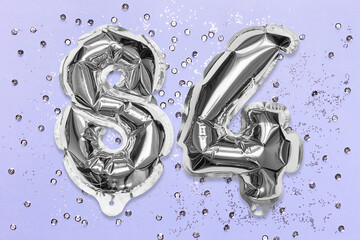 Silver foil balloon number, digit eighty four on a lilac background with sequins. Birthday greeting card with inscription 84. Top view. Numerical digit. Celebration event, template.