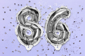 Silver foil balloon number, digit eighty six on a lilac background with sequins. Birthday greeting card with inscription 86. Top view. Numerical digit. Celebration event, template.