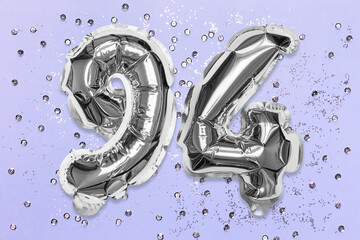 Silver foil balloon number, digit ninety four on a lilac background with sequins. Birthday greeting card with inscription 94. Top view. Numerical digit. Celebration event, template.