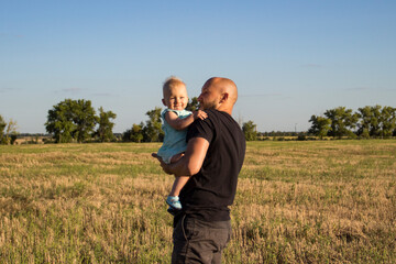 Young man holds a child in his arms against the background of the field. Concept game with children, happy family