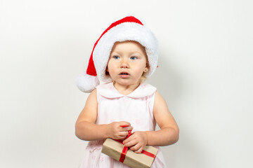 Little child in a hat of Santa Claus holds a gift on a light background. Banner. Gifts concept for christmas and winter holidays, happy family