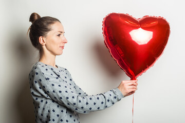 Young woman in a sweater looks at the Heart air balloon on a light background. Valentines day concept