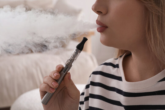 Young woman using electronic cigarette at home, closeup