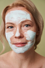 Satisfied woman enjoying of her clay face mask while posing with bare shoulders