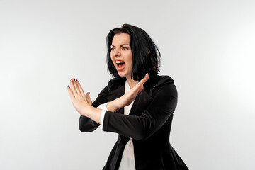 Serious young businesswoman in black formal jacket white shirt shows cross stop gesture with an angry aggressive expression, standing over white background. Business concept