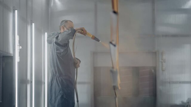 A man in a respirator is painting metal with a powder method. Production of steel and metal structures. Painting shop. The painter works with a spray gun paint 