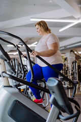 Fototapeta na wymiar Happy mid adult overweight woman exercising on stepper indoors in gym