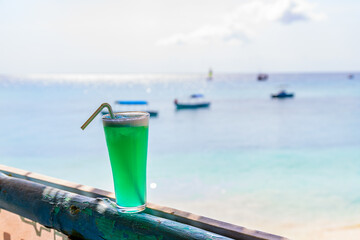 Glass of blue hawaii cocktail. Ocean at the background