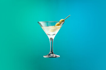 Cocktail glass with dry martini with olives isolated over gradient blue green color background in neon.
