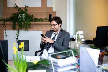 Smiling handsome freelancer working remotely from home office. He is speaking on the phone.