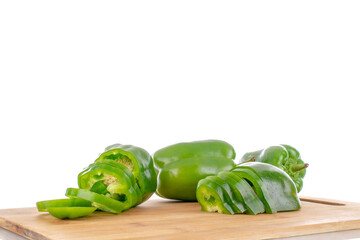 Two half juicy sweet green peppers cut into slices and two whole peppers on a wooden board, close-up, isolated on white.