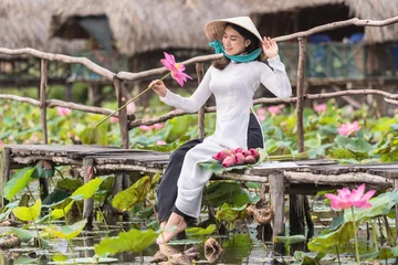 Poster Portrait of beautiful vietnamese woman with traditional vietnam hat holding the pink lotus on the wooden bridge in big lotus lake, vietnam, aisan or southeast asia travel concept © THANANIT