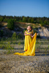 Beautiful blonde girl posing in a yellow dress in nature. Summer photo. Blue sky. Sunny day.
