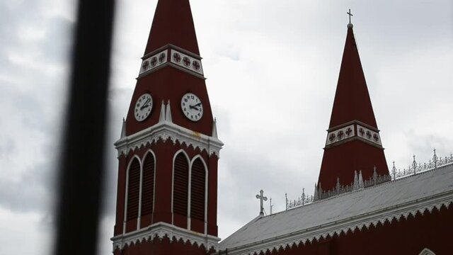 Red iconic chapel on an overcast day in Grecia, Costa Rica. Templo Nuestra Se&ntilde;ora de las Mercedes. Only metal church in central America. Trucking sideways camera movement behind bars of steel fence