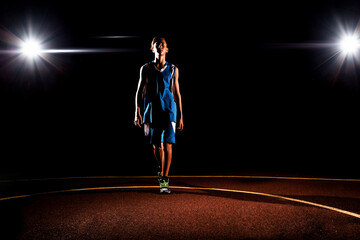 Fototapeta na wymiar Basketball. A teenage boy in blue sportswear on the Playground. There are two spotlights in the background. Black background. Concept of sports games