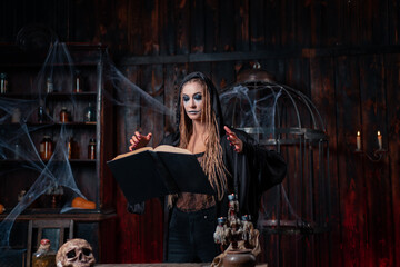 Fototapeta na wymiar Halloween concept. Witch dressed black hood with dreadlocks standing dark dungeon room use magic book for conjuring magic spell