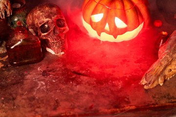 Halloween. Scary Halloween pumpkin with carved face on table in dark room with human skull and...