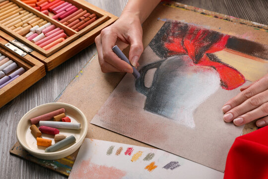 Woman drawing beautiful jug with soft pastel at wooden table, closeup