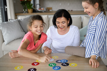 Happy small girls with grandmother playing cards indoors at home.