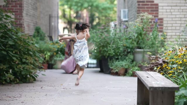 A little girl runs and skips running towards a photographer taking her picture in a lush green garden on a summer day outside