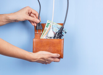 Woman hand puts electric power plugs in open wallet with Euro banknotes. Energy efficiency, power...