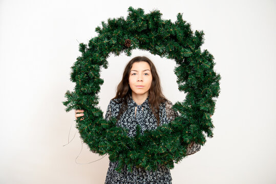  Smiling young woman looking through a green Advent Christmas wreath on a white background