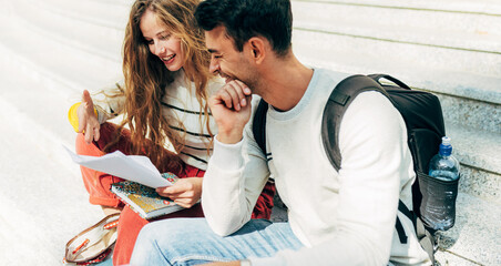 Horizontal image of a two young university students studying sitting on the stairs of the college campus. Woman and man sitting outside learning together from the books.