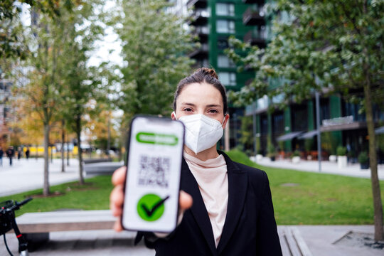 Businesswoman wearing protective mask showing COVID-19 vaccine certificate on smart phone