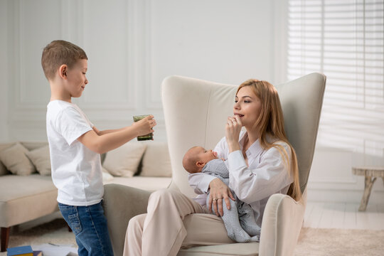 The mother holds the child in her arms and drinks vitamins. The eldest son brings his mother a glass of water.