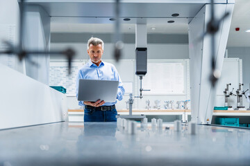 Engineer with laptop at automated manufacturing machinery in industry