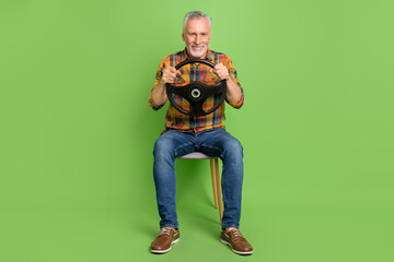 Full length photo of funny aged beard man sit drive auto wear shirt jeans sneakers isolated on green color background