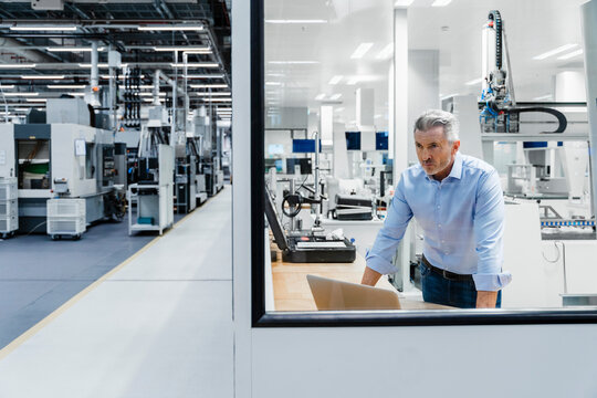 Confident businessman looking through glass at factory - Powered by Adobe