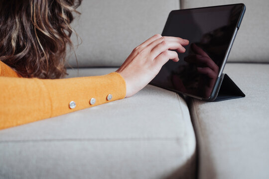 Woman touching tablet PC screen on sofa at home