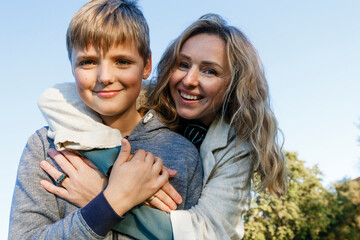Happy blond woman embracing son in park