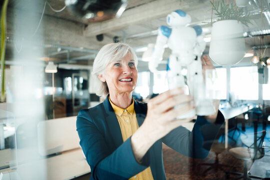 Senior businesswoman holding robot toy in office