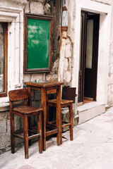 Fototapeta na wymiar Wooden high table and two chairs near the wall of a small bar on the street