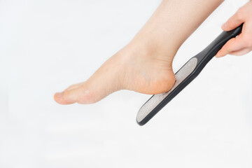 Women's foot on a white background, polishing the heel with a file, pedicure in the salon or at...