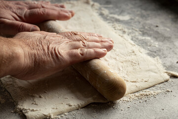 Man rolling out a sheet of puff pastry.  On a concrete surface