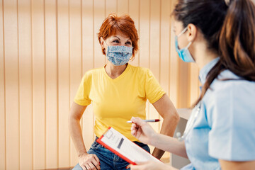Healthcare, insurance, and medical service. A woman with a mask sitting in a doctor's office and...