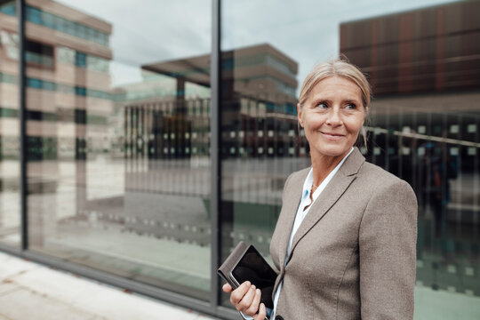 Businesswoman holding tablet PC in front of glass wall