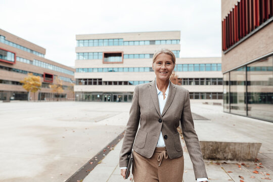 Smiling businesswoman with tablet PC walking on footpath