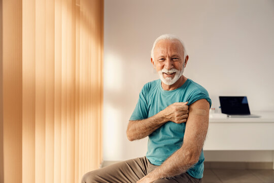 Vaccination for elders. A happy senior man sitting in the doctor's office and showing his arm with adhesive plaster after covid 19 vaccine.