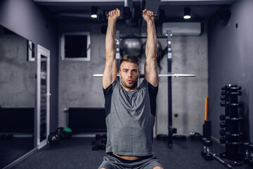 Fototapeta premium The athlete trains dumbbells in the gym on a dark grey background. Sport concept and taking care of the figure. The man lifts dumbbells, cares for his muscles. Weightlifting, sports training