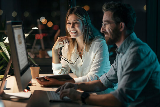 Smiling businesswoman with digital tablet by colleague working on computer at office