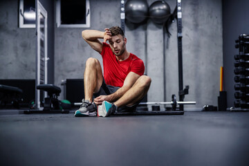 Exhaustion in training. The man sits on the floor of the gym and rests between exercises. He is...