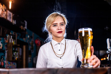 Charismatic woman bartender formulates a cocktail while standing near the bar counter in pub