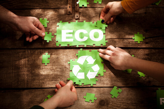Friends joining ECO word and recycling symbol on table