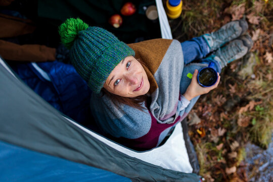Smiling woman wrapped in blanket holding coffee mug inside tent